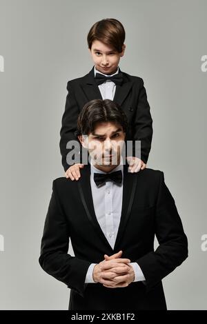 Un padre e un figlio, entrambi in costume nero, posano per una foto. Il figlio è seduto sulle spalle dei suoi padri. Foto Stock