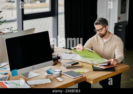 Un uomo d'affari con il barbuto che indossa gli occhiali siede alla sua scrivania in un ufficio moderno, rivedendo attentamente i documenti. Foto Stock