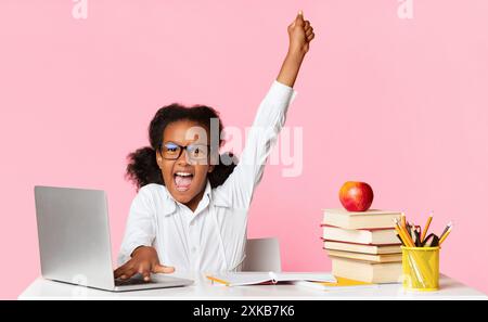 Afro Schoolgirl alzando la mano seduti al computer portatile in Studio Foto Stock