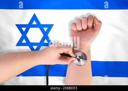 Primo piano di una testa di stetoscopio medico su un polso con la bandiera israeliana sullo sfondo. Concetto del sistema sanitario israeliano Foto Stock