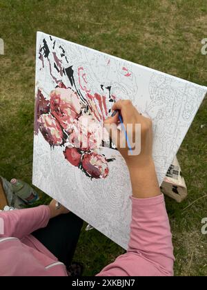 La donna scrive un'immagine per numeri. Pitture in barattoli numerati e una lattina d'acqua. All'aria aperta. Primo piano. Foto Stock