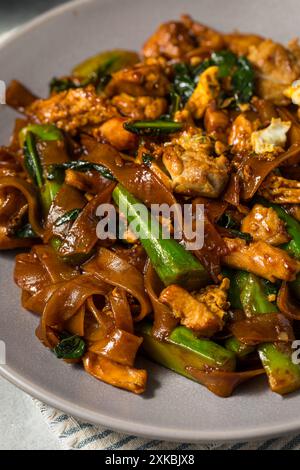 Salato cuscinetto asiatico ammira gli spaghetti alle erbe con pollo e broccoli Foto Stock