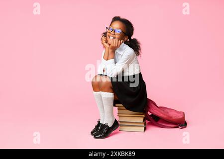 Sorridente livellatrice prima ragazza seduta sulla pila di libri in Studio Foto Stock