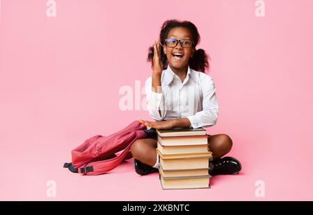 Nerdy Schoolgirl alzando la mano seduta a Libri su sfondo giallo Foto Stock