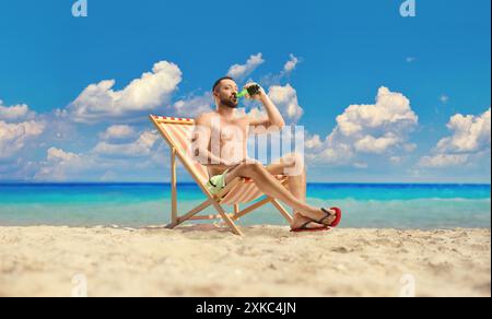 Uomo che beve birra su una spiaggia in riva al mare Foto Stock