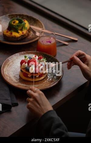 Le mani di una donna tagliano un pancake. Pancake servito con frutti di bosco e panna montata sul tavolo del ristorante. Foto Stock