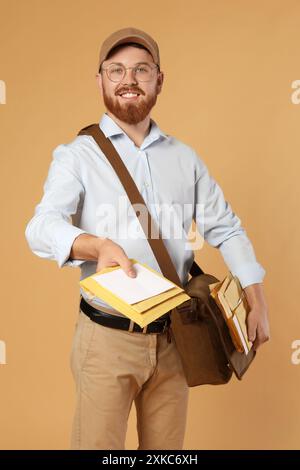 Felice giovane postino con borsa in pelle che consegna lettere su sfondo marrone Foto Stock