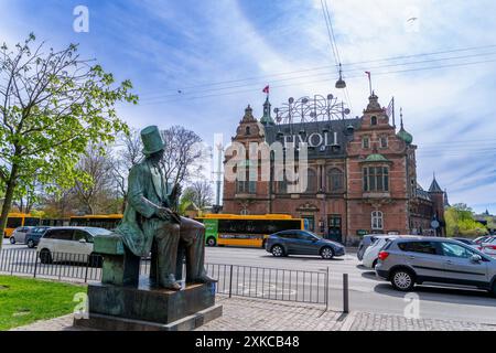 Copenaghen, Danimarca - 29 aprile 2024: Una statua di bronzo di Hans Christian Andersen si trova con un libro in mano, guardando verso i giardini di Tivoli. Foto Stock