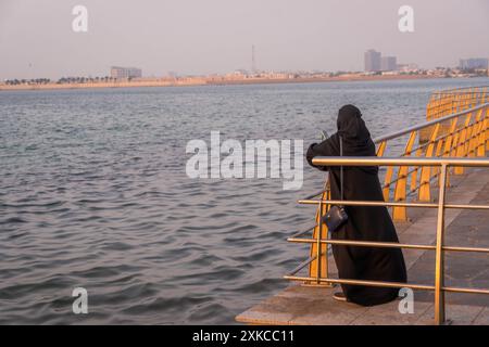 La paranja copriva la donna musulmana sulla Jeddah Corniche (lungomare) in Arabia Saudita che guardava il bellissimo tramonto in Medio Oriente. Foto Stock