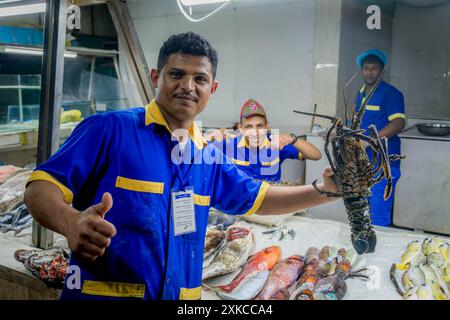 Il felice venditore di pesce saudita al mercato del pesce di Jeddah, che mostra aragosta e pollice al banco di pesce in Arabia Saudita. Foto Stock