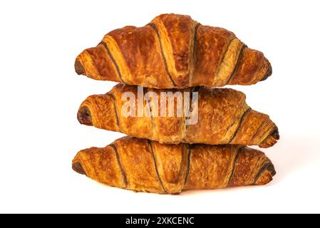 Un trio di croissant perfettamente cotti, marrone dorato e scaglie, sono impilati su uno sfondo bianco. I croissant hanno una leggera lucentezza e strati visibili Foto Stock