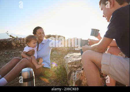 Una famiglia ama fare un picnic all'aperto e sorseggiare un tè in collina. La scena ritrae calore, felicità e solidarietà in natura. Foto Stock