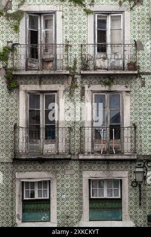 Primo piano della classica facciata in piastrelle portoghesi e dei balconi con finestre francesi in un edificio di appartamenti abbandonato e fatiscente nel centro di Lisbona, a Portug Foto Stock