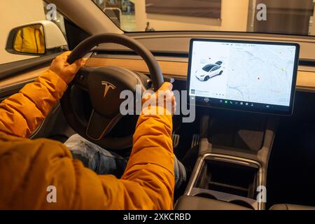 Primi piani maschili mani sul volante, auto elettrica Tesla modello Y Interior, abitacolo tecnologie EV moderne produzione di auto, come autopilota, eco-frie Foto Stock