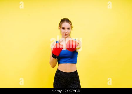 Giovane donna stanca con abbigliamento sportivo e guanti da boxe in piedi isolata su sfondo bianco giallo. Foto Stock