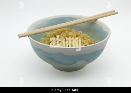 Spaghetti istantanei nel recipiente con bacchette su sfondo bianco Foto Stock