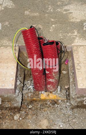 Immagine di due tubi corrugati rossi legati insieme in una struttura in cemento, con un cavo giallo avvolto intorno a uno di essi, in un ambiente di costruzione. Foto Stock