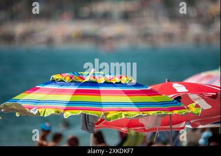 Su una spiaggia pubblica spagnola, i turisti amanti del sole affollano la zona di colori in una calda giornata estiva con molti ombrelloni. Immagini ad alta risoluzione di un ragazzo dentro Foto Stock