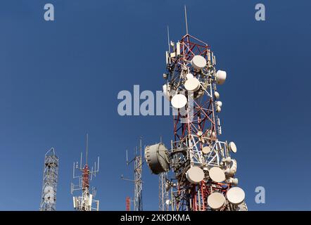 Un'alta torre di comunicazione con molte antenne in cima. Il cielo è blu e limpido. La torre è circondata da altre torri. Foto Stock