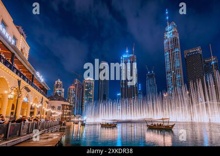 Le persone si godono un giro in barca mentre guardano uno spettacolo della Fontana di Dubai di notte, con i grattacieli di Dubai sullo sfondo. Foto Stock