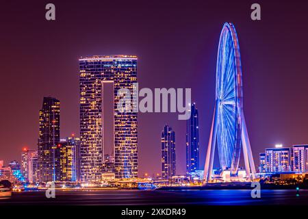 Una ruota panoramica si erge illuminata contro il cielo notturno, circondata da grattacieli a Dubai. Foto Stock