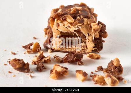 Barretta di wafer di cioccolato rotta con noci e caramello tagliati e briciole isolate su sfondo bianco Foto Stock