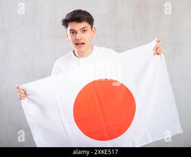 Lo spettatore maschio attivo e pieno di energia tiene in mano la bandiera nazionale del Giappone e canta slogan popolare. Foto Stock