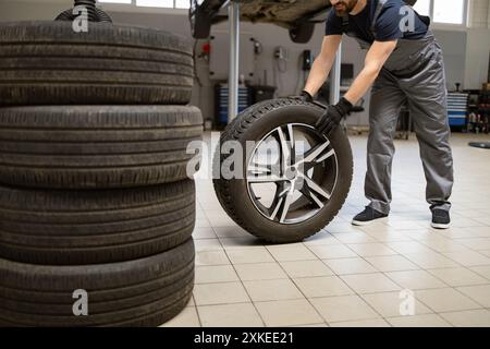 Meccanico che maneggia gli pneumatici in officina di riparazione Foto Stock