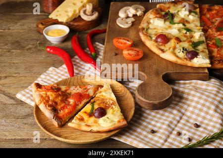 Piatto con diverse fette di pizza, ingredienti e utensili da cucina su fondo in legno Foto Stock