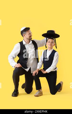 Felice padre ebreo che mette il cappello sul suo figlioletto su sfondo giallo Foto Stock