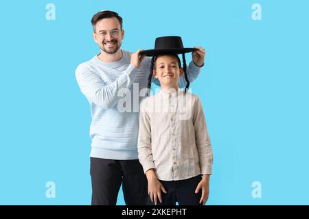 Felice padre ebreo che mette il cappello sul suo figlioletto su sfondo blu Foto Stock