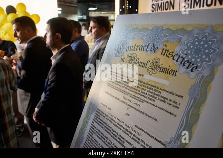 Bucarest, Romania. 22 luglio 2024: George Simion (L), il candidato del partito populista e nazionalista di destra AUR (Alleanza per l'Unione dei rumeni), parla alla stampa durante una campagna elettorale, accanto a un grande cartello che raffigura "il contratto di iscrizione al piano Simion" che la gente è invitata a firmare, presso la sede della sua campagna nel negozio di Bucarest. Il "piano Simion" mira ad agevolare l'acquisto senza interessi di un appartamento a partire da 35.000 euro e il rifinanziamento, a zero interessi e altri costi interamente sovvenzionati dallo Stato, del mutuo esistente loa Foto Stock