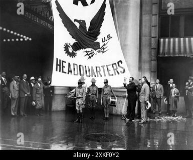 New York, New York 21 agosto 1933 nemmeno un downpour poteva fermare le cerimonie di innalzamento della bandiera dell'NRA presso l'Hotel Pennsylvania, dato che un enorme striscione della National Recovery Administration è stato innalzato in una posizione di rilievo davanti all'hotel. Grover Whalen, presidente della campagna di New York City, è mostrato mentre officiava, mentre diversi funzionari della città e una piccola folla, tenuti al minimo dalla pioggia, guardavano. Foto Stock