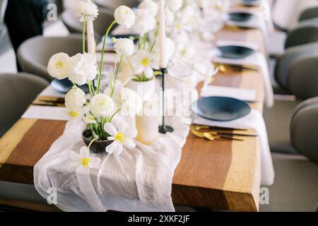 Mazzi di fiori bianchi si stagliano su un tessuto stretto su un tavolo festivo con piatti neri Foto Stock