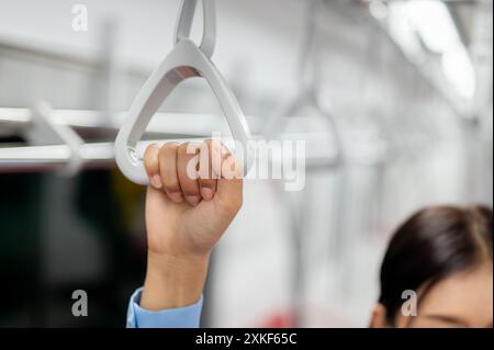 Immagine ravvicinata della mano di una donna che tiene il corrimano in un treno sopraelevato o in una metropolitana, che viaggia con i mezzi pubblici in una città movimentata. Metro, BTS, u Foto Stock