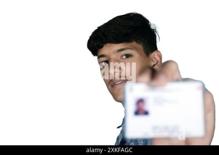 Il ragazzo di scuola indiano che indossa l'uniforme blu scuro della scuola, con il viso sorridente mostra la sua carta aadhar sfocata in mano. Foto Stock