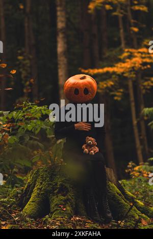 donna spaventosa con testa di zucca nella foresta con giocattolo Foto Stock