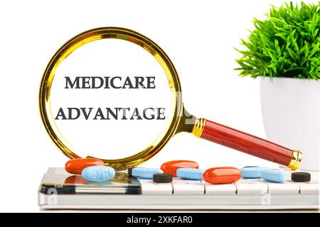 Testo Medicare Advantage attraverso una lente d'ingrandimento in una composizione con una calcolatrice, compresse e una pianta su sfondo bianco Foto Stock