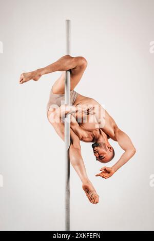 L'uomo muscolare tiene con grazia una posa di pole dance, mostrando forza e flessibilità Foto Stock