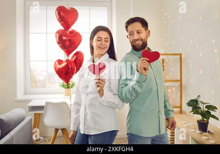 Ritratto di una giovane coppia felice che tiene in mano i cuori di carta rossa mentre celebra San Valentino. Foto Stock