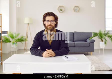 Serio uomo d'affari con la barba seduto al tavolo in un ufficio moderno Foto Stock