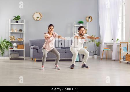 Giovane coppia felice e sportiva che indossa abbigliamento sportivo e si allena nel salotto di casa. Foto Stock