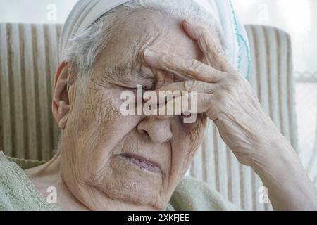 Una donna anziana che piange in una poltrona Foto Stock