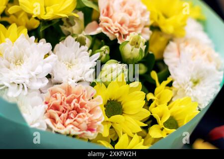 Il bouquet consiste di vibranti fiori gialli e rosa disposti in modo ordinato e racchiusi in un involucro di carta verde fresca, creando una deliziosa esposizione Foto Stock