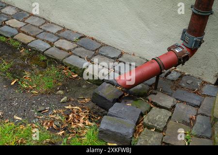 Un tubo rosso che esce dal muro, ed è legato ad un vecchio sistema di acqua piovana grigia su ciottoli nel cortile anteriore. Primo piano. Foto Stock