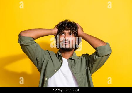 Foto ritratto di un giovane ragazzo latino in camicia cachi depresso ubriaco toccando la testa sofferente isolato su sfondo di colore giallo Foto Stock