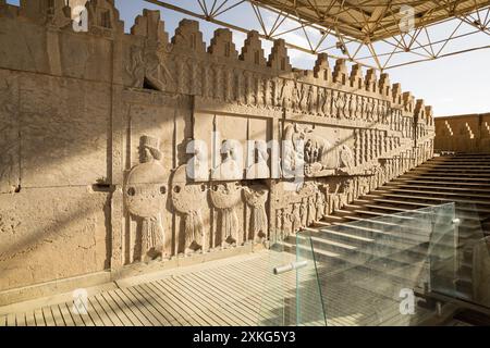 Sculture in rilievo di soldati in rilievo accanto a un leone che caccia un toro su una delle scale a Persepoli, l'antica capitale persiana vicino a Shiraz, Iran Foto Stock