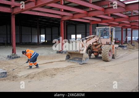 Costruzione dell'hangar. Bulldozer in funzione, uomo lavoratore che scava con una pala. 20 marzo 2019. Berezovka, Ucraina Foto Stock