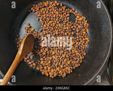 Primo piano di chicchi di caffè tostati in una padella con un cucchiaio di legno Foto Stock