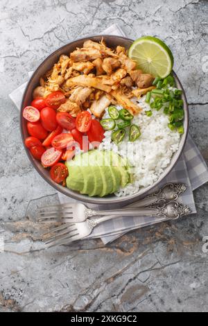 Piatto di riso messicano con carnitas di pollo, pomodori ciliegini, avocado, peperoni da vicino sul tavolo. Vista dall'alto verticale Foto Stock